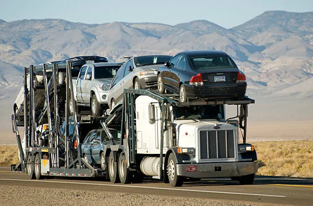 Open car carrier loaded with cars and a pickup truck on a desert highway