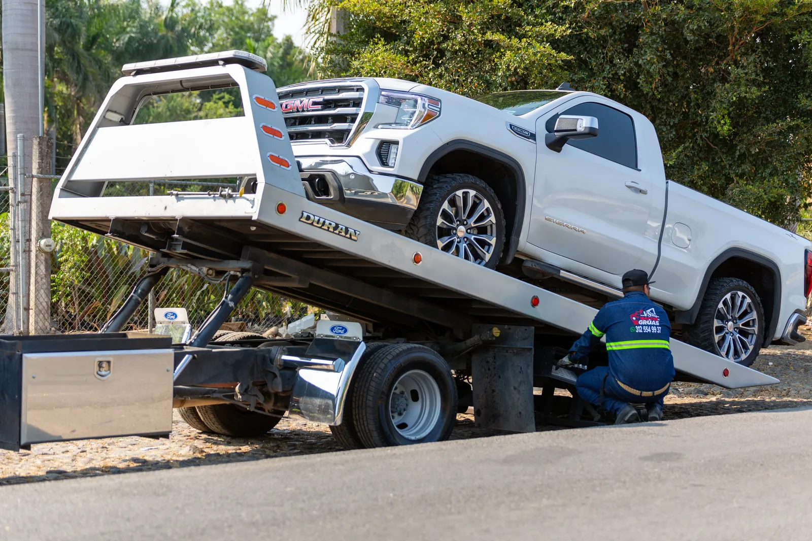 White GMC Sierra pickup being winched onto a rollback flatbed truck for transport