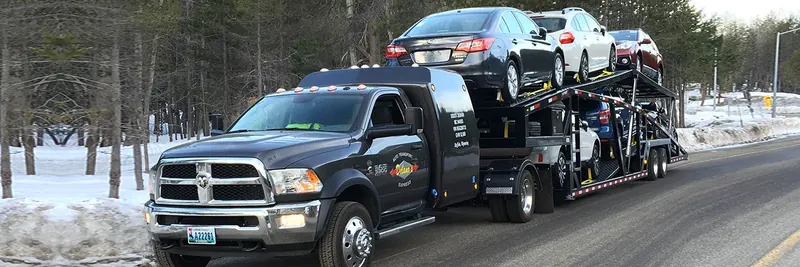 Ram dually truck pulling a three-car trailer loaded with vehicles on a snowy road